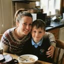 A mum at the kitchen table with her arm around her son, his school bag beside them.
