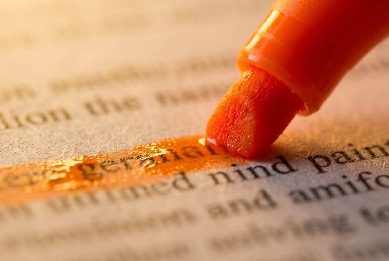 Extreme close-up of an orange highlighter tip marking one line of printed text on a paper document, the surrounding print blurred