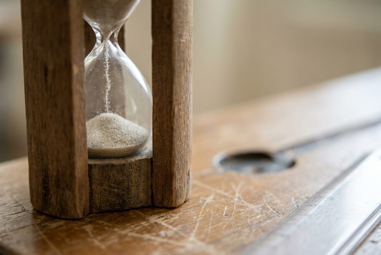 Extreme close-up of a small sand timer on a scuffed classroom desk, the grains caught mid-fall in a narrow plane of focus.