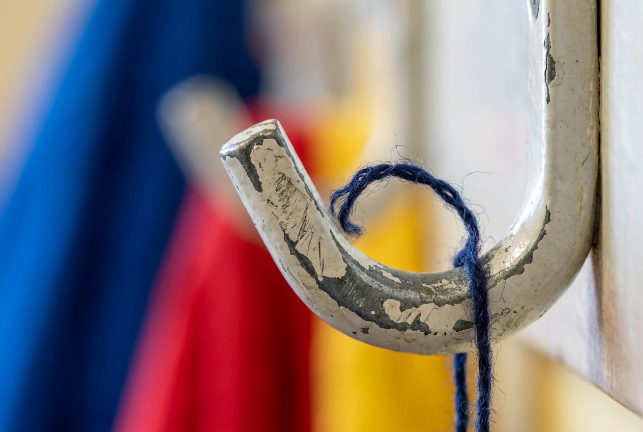 Extreme close-up of a bare, chipped coat hook on a school cloakroom rail, with a single loose wool thread caught on it.