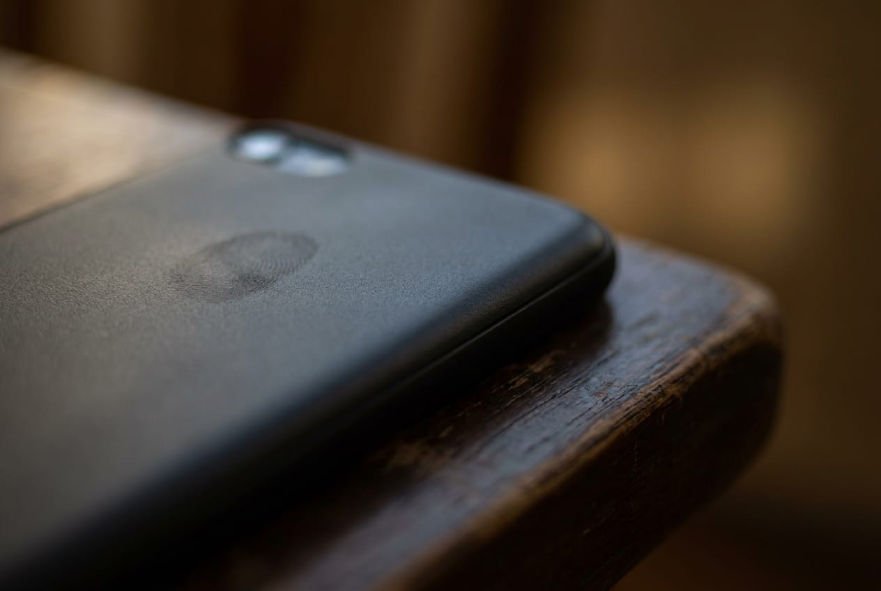 Extreme close-up of a switched-off mobile phone lying face down on a bare wooden table, the edge of the phone and the grain of the wood filling the frame